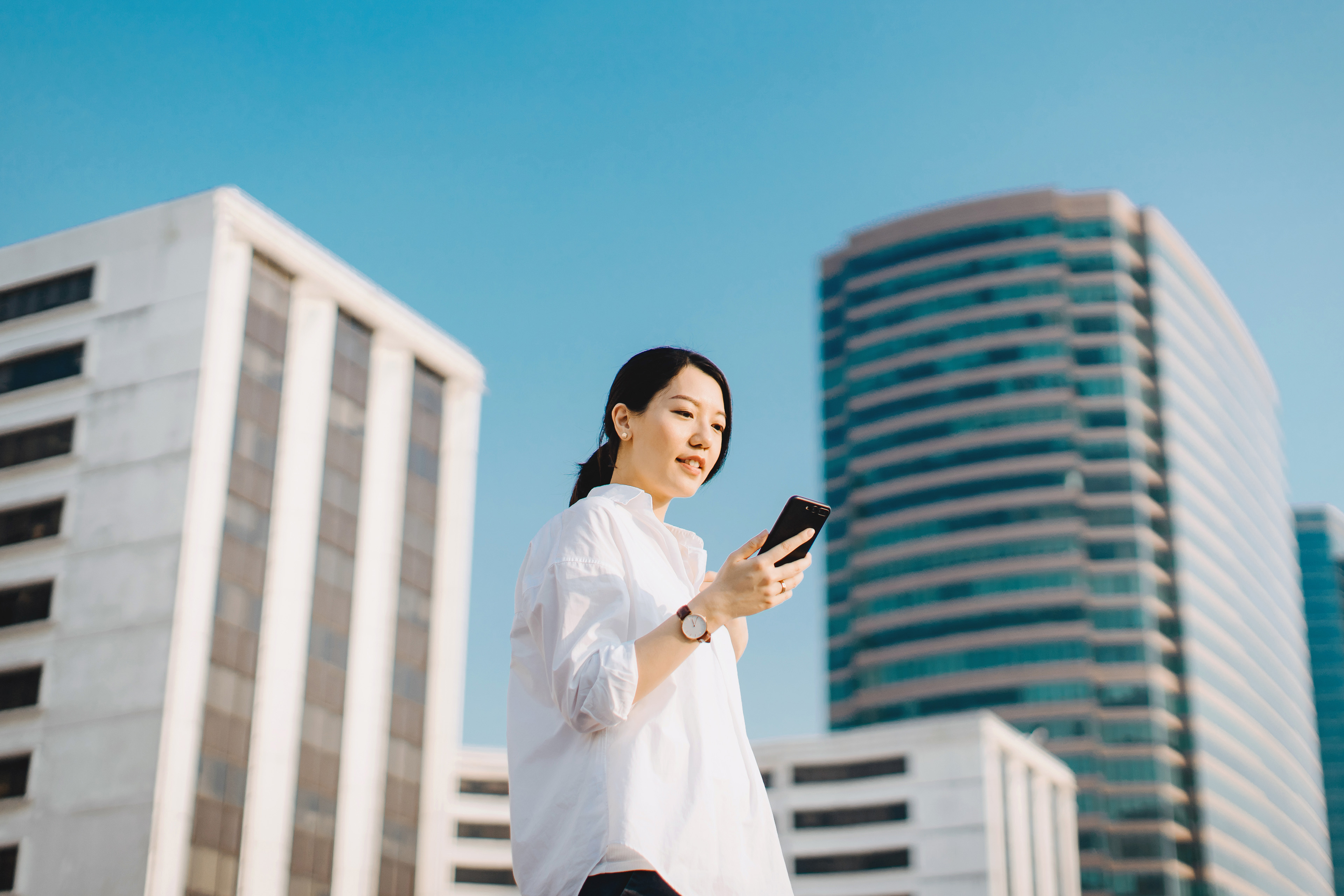 Confident young woman emailing on smartphone in city