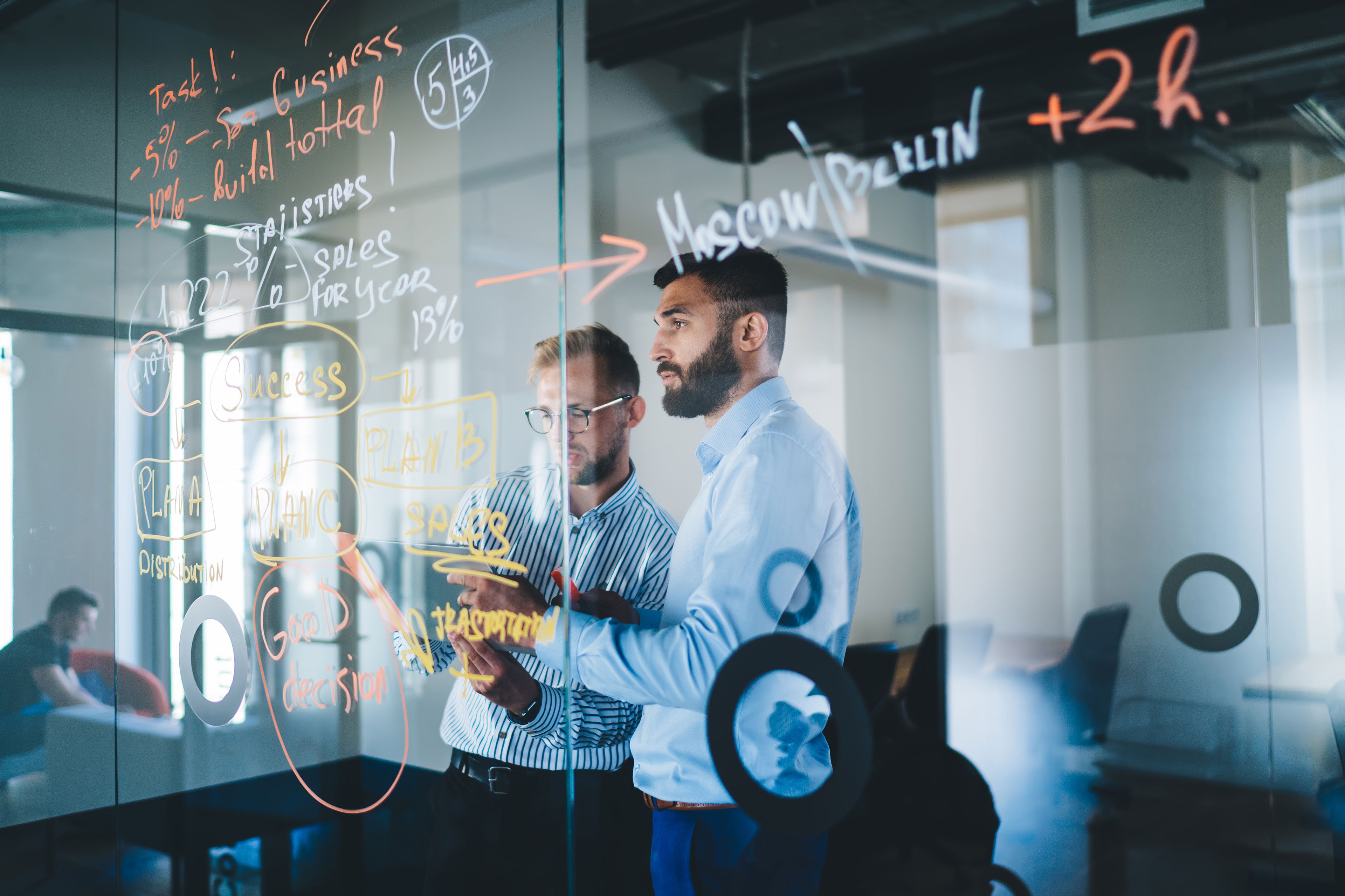 Two businessmen writing on glass board