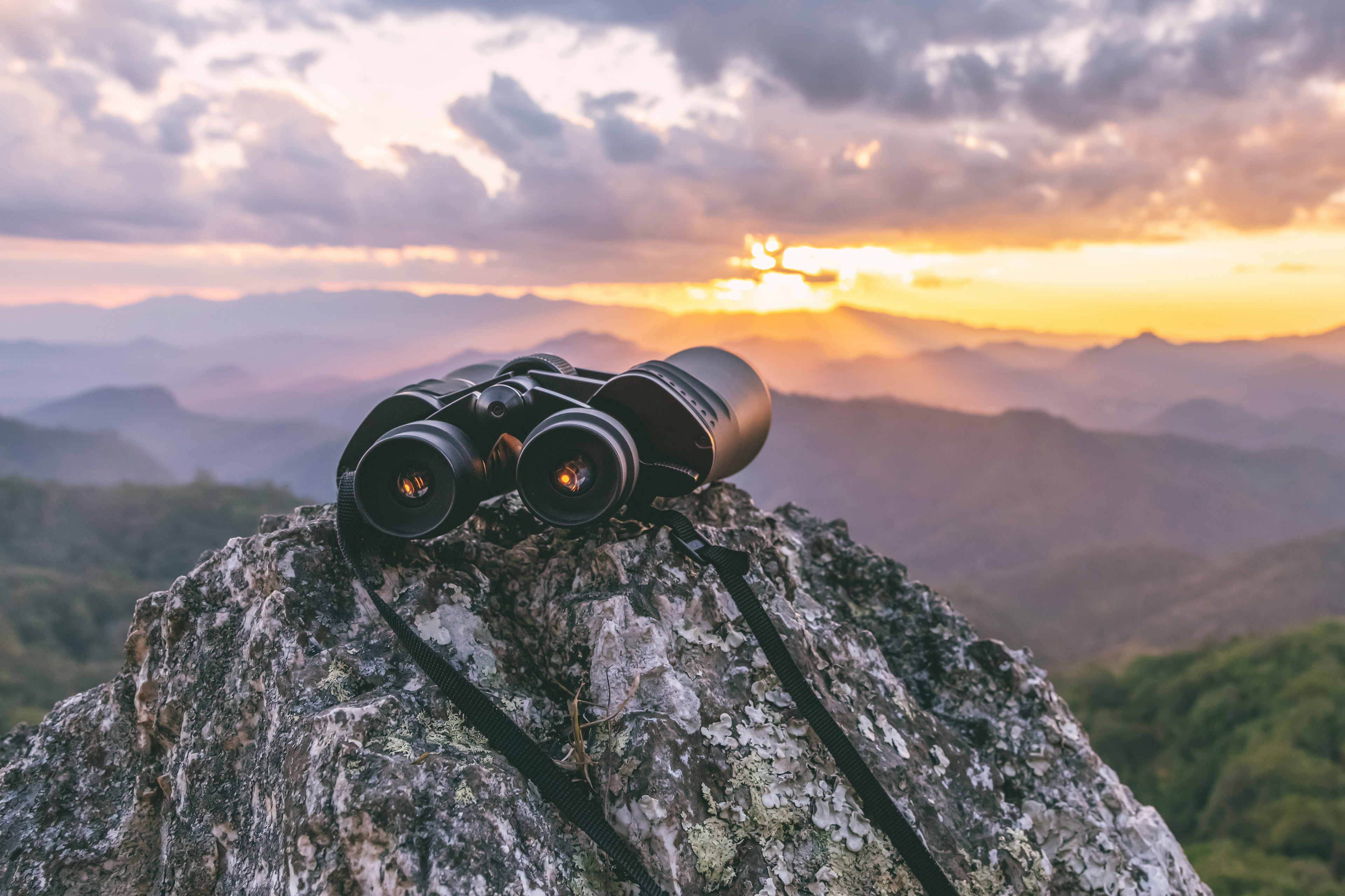 Binoculars on top of rock mountain at sunset