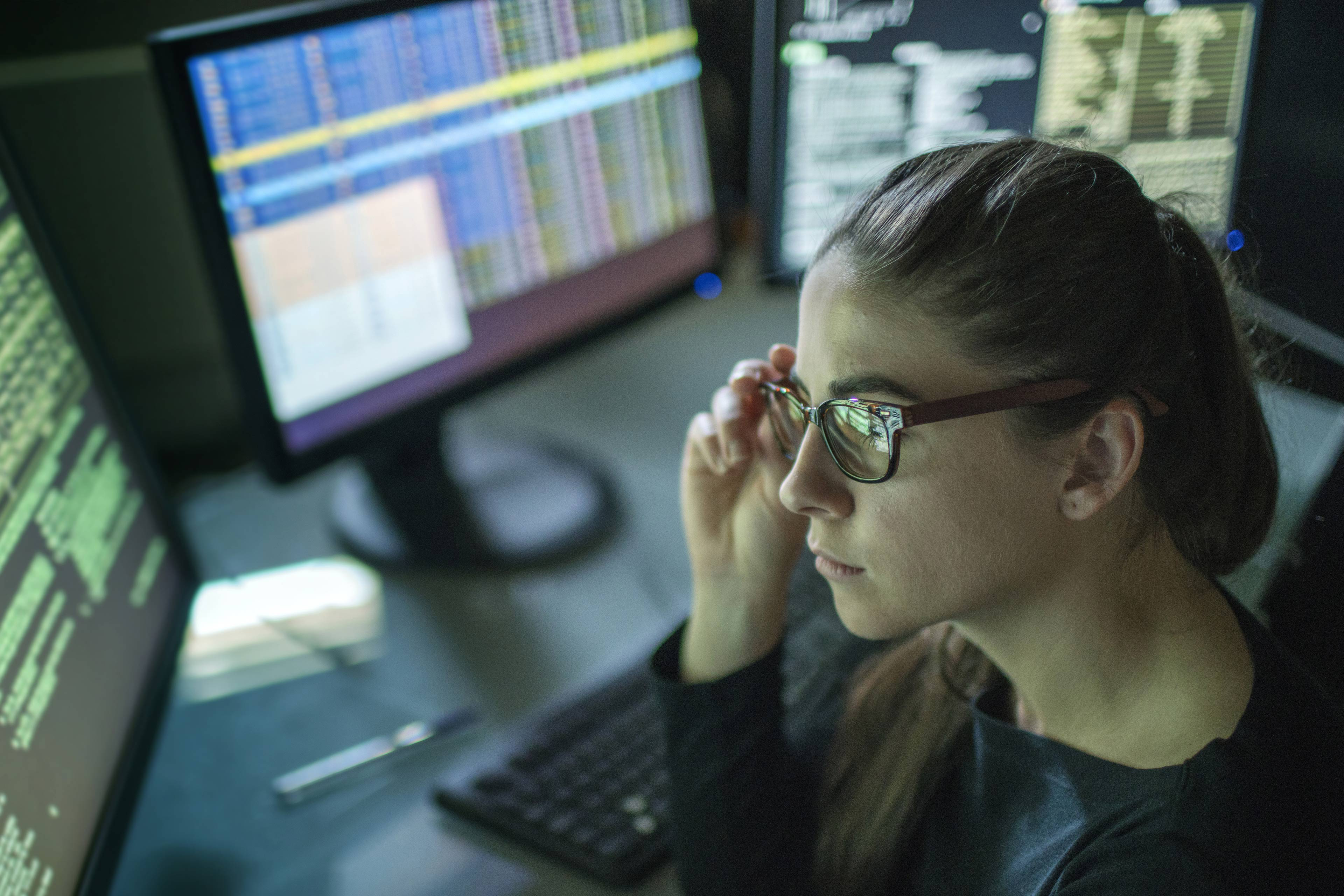 woman seated at desk surrounded by monitors displaying data