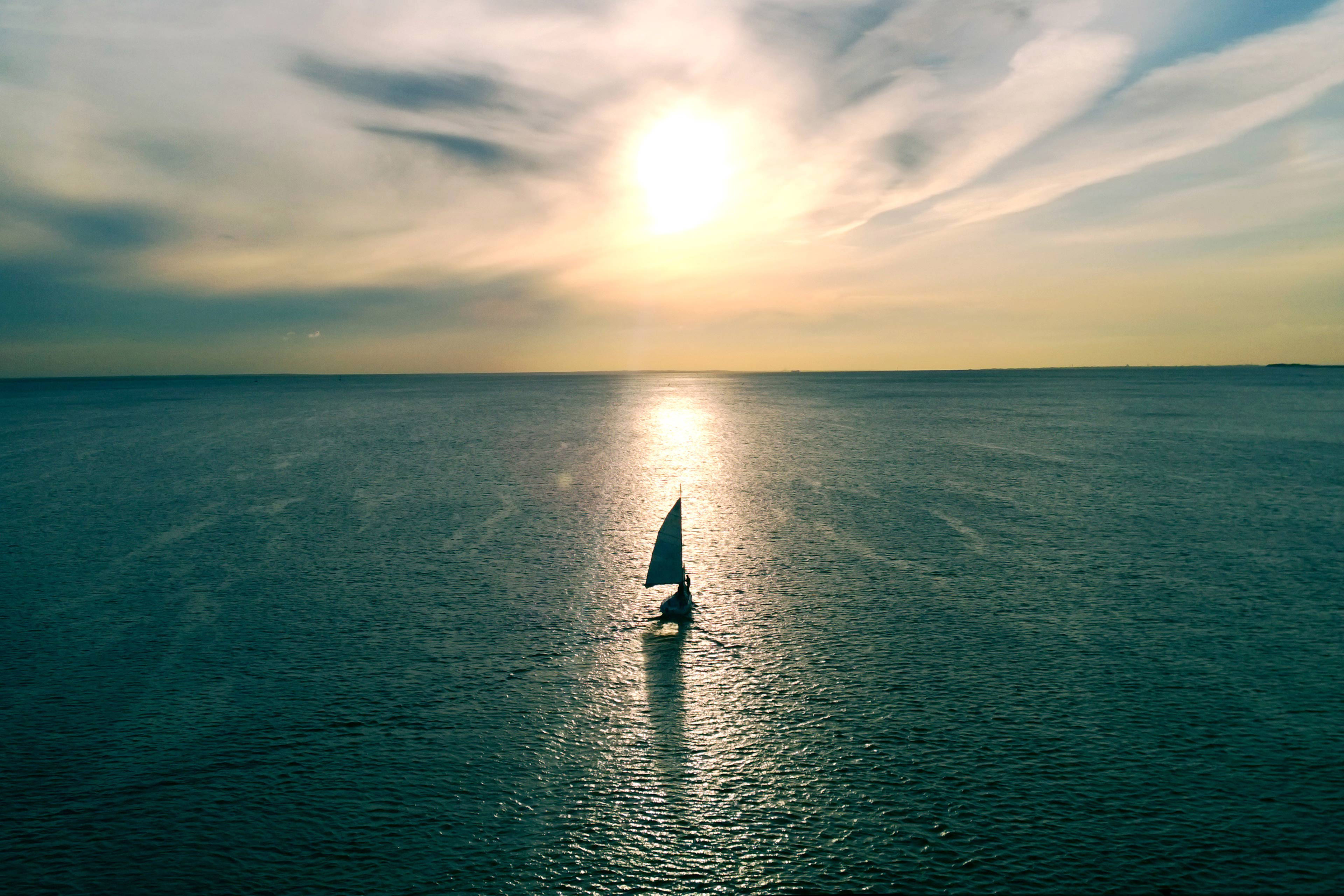 Sailboat floating on the water towards the horizon in the rays of the setting sun