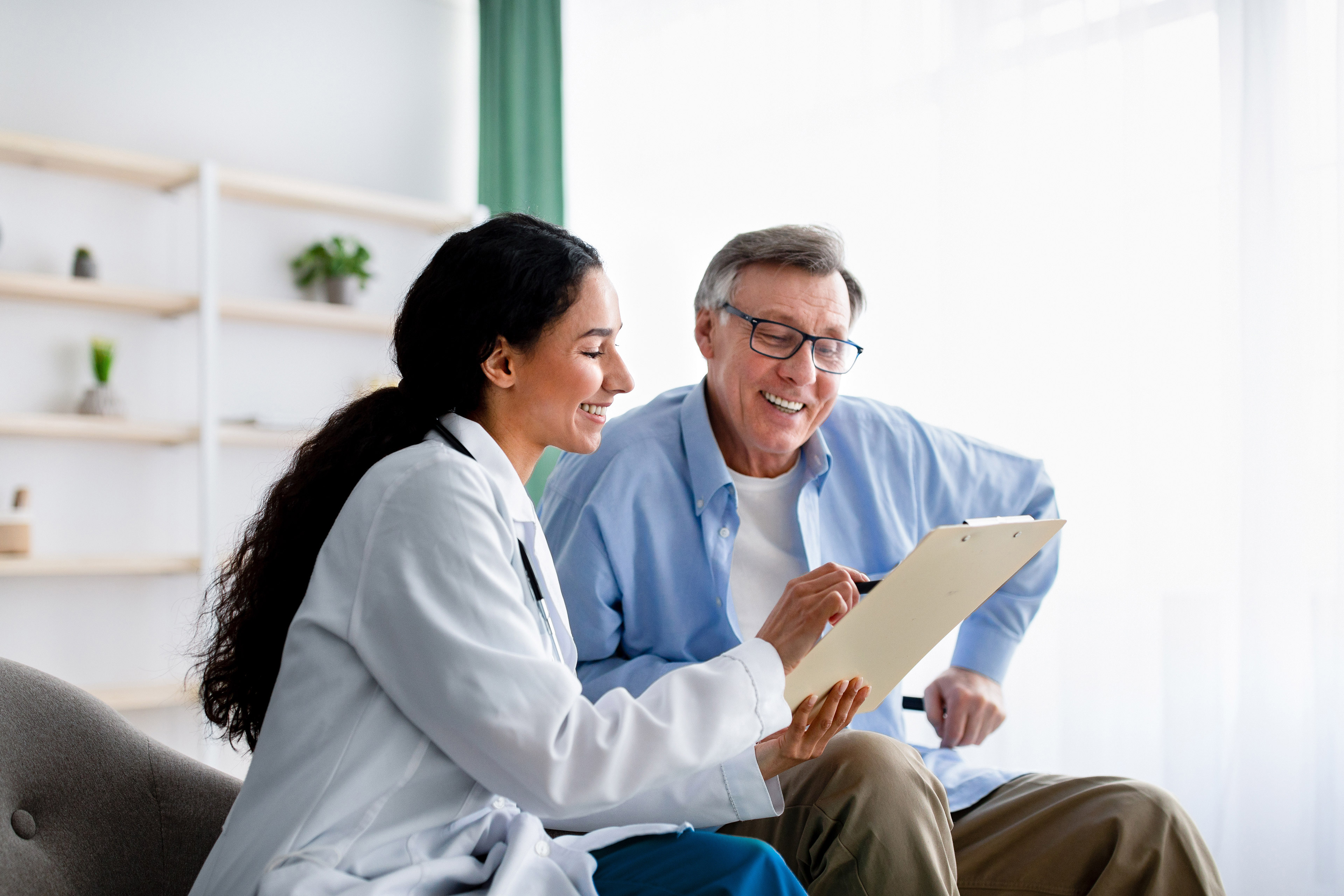 Young doctor asking senior impaired male patient in wheelchair to sign insurance policy at home