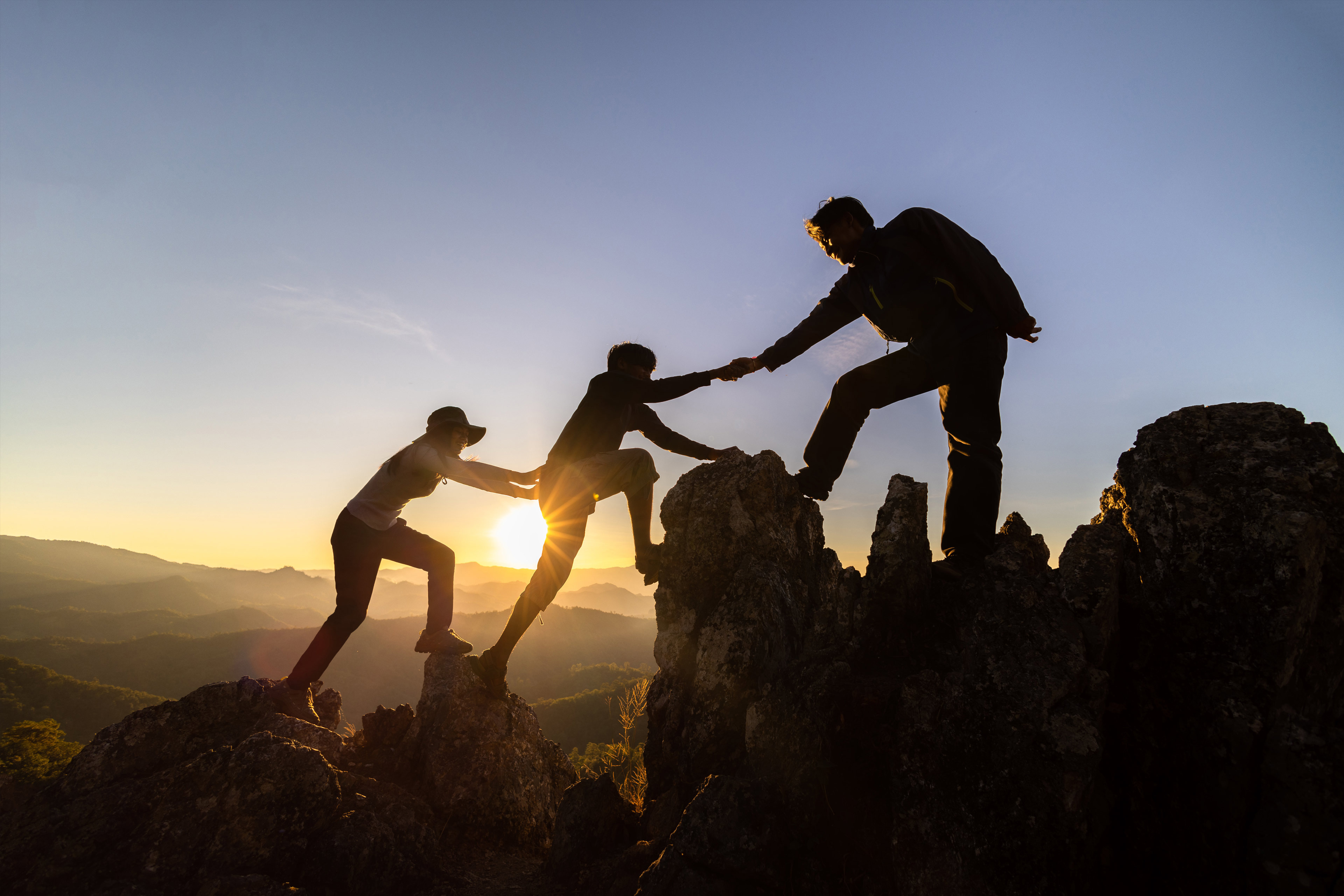 Teamwork three hikers helping each other to the top of the mountain