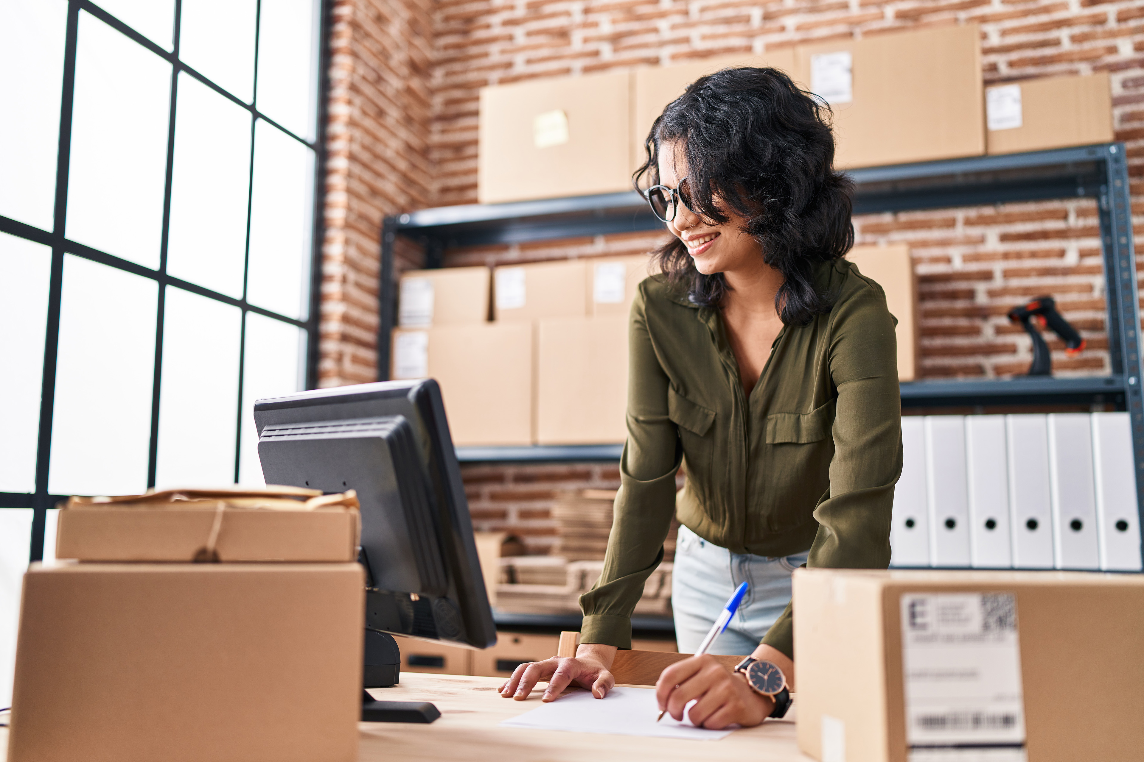 Young latin woman ecommerce business worker writing on paper at office