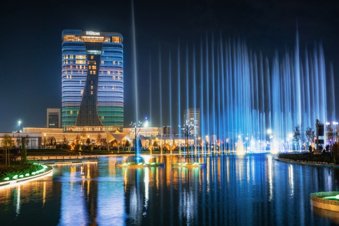 Dancing fountain illuminated at night with reflection in pond in new Tashkent City Park