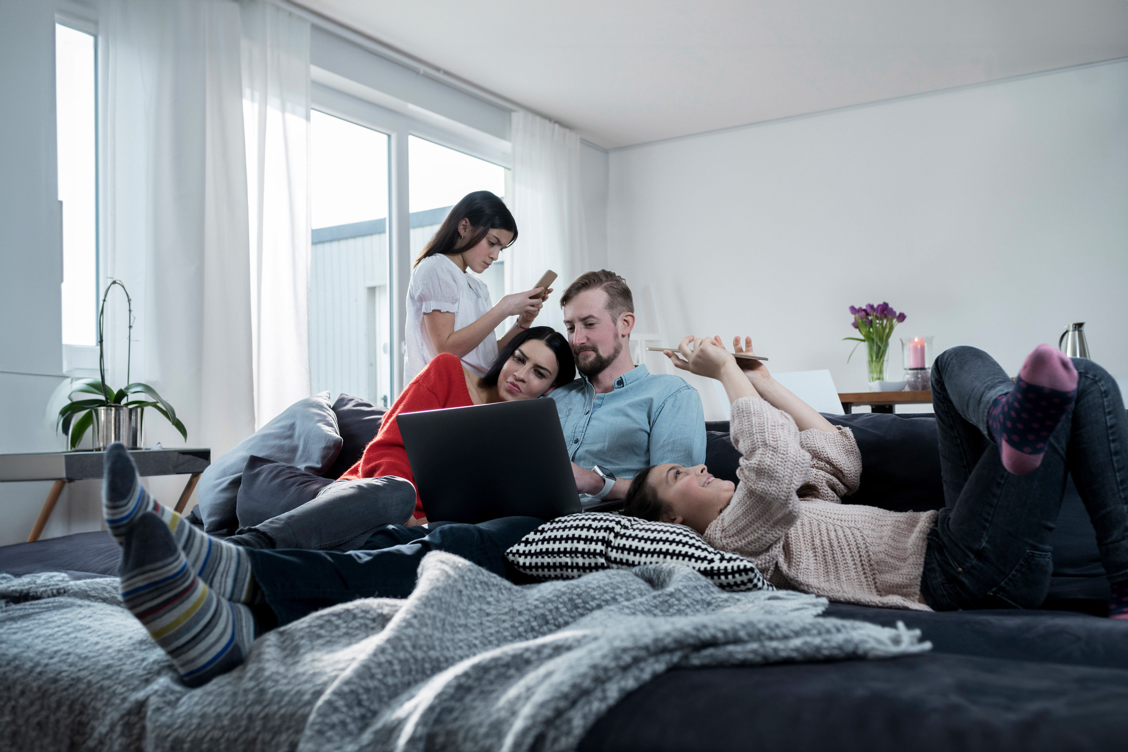 Parents and twin daughters on sofa using portable devices