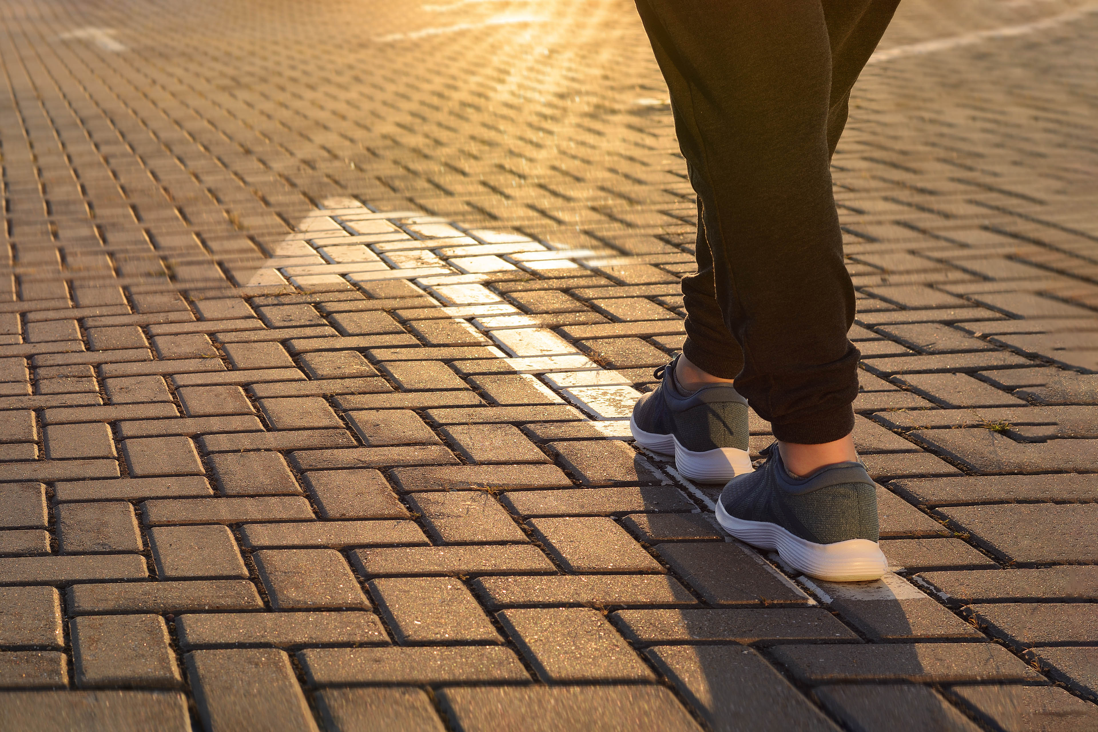 Forward moving. Feet on road white arrow in the rays of setting sun closeup. 