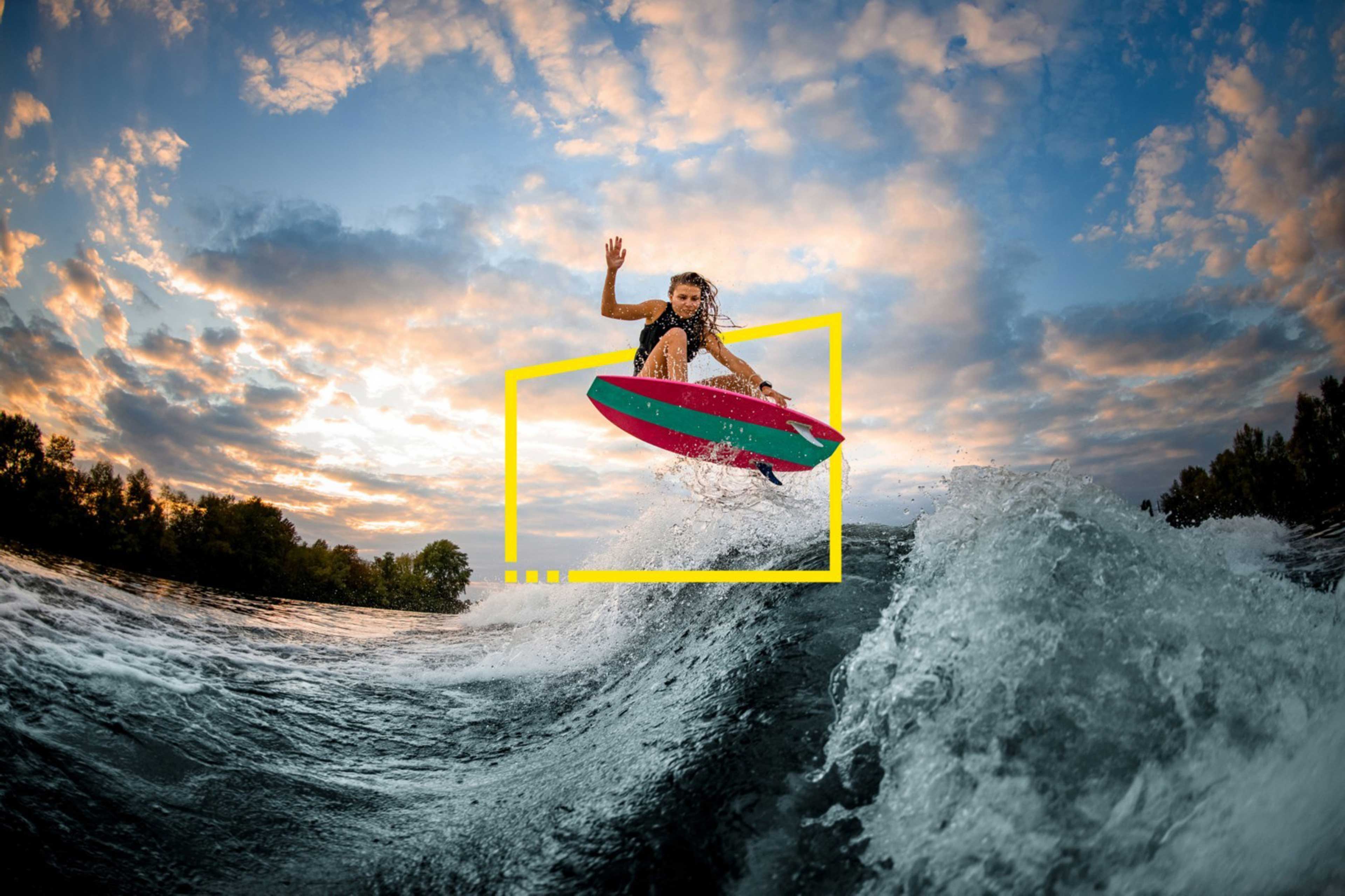 Woman jumping over a big splashing wave on surf style wakeboard