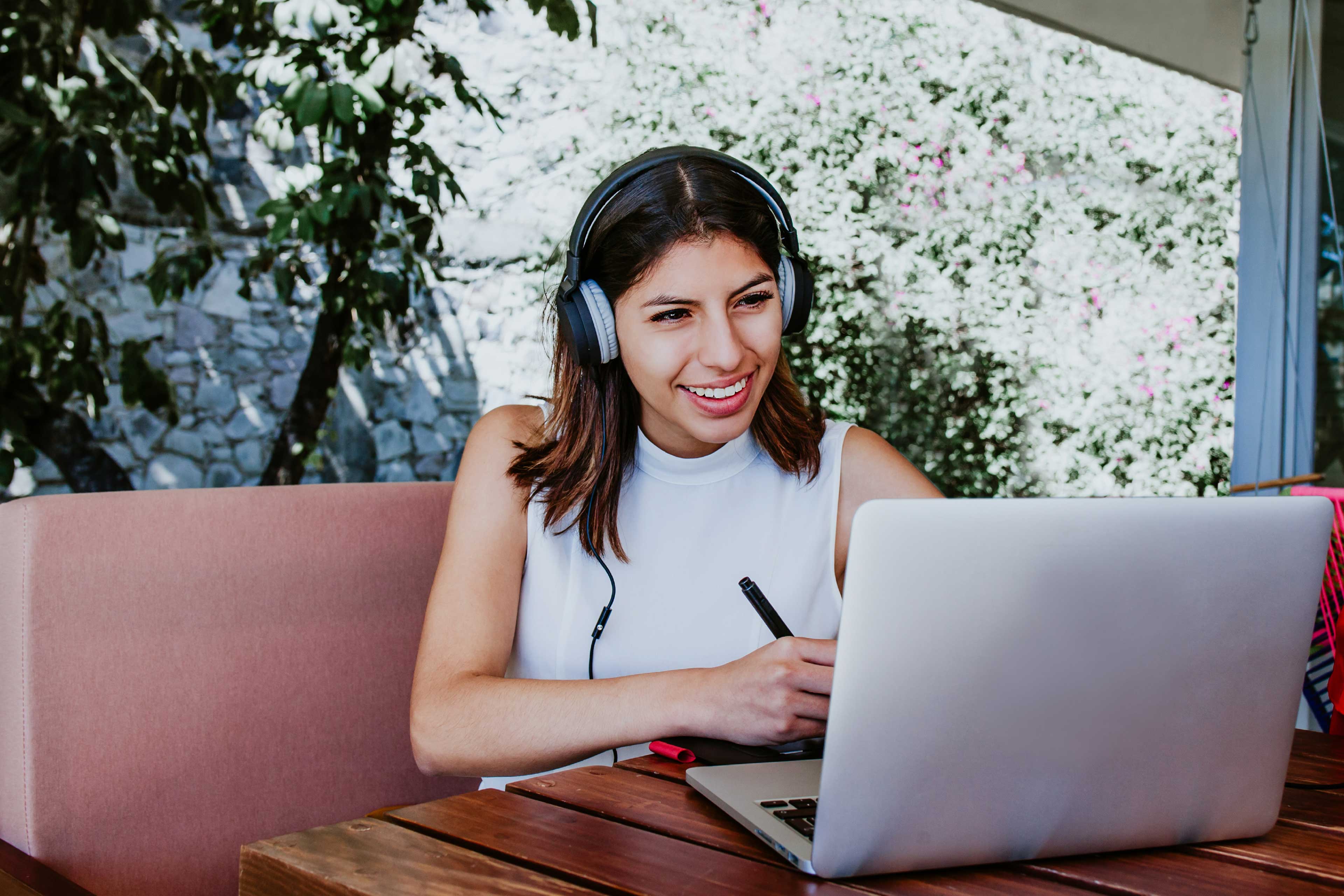 Mujer trabajando en su casa con auriculares puestos y sonriendo a la computadora