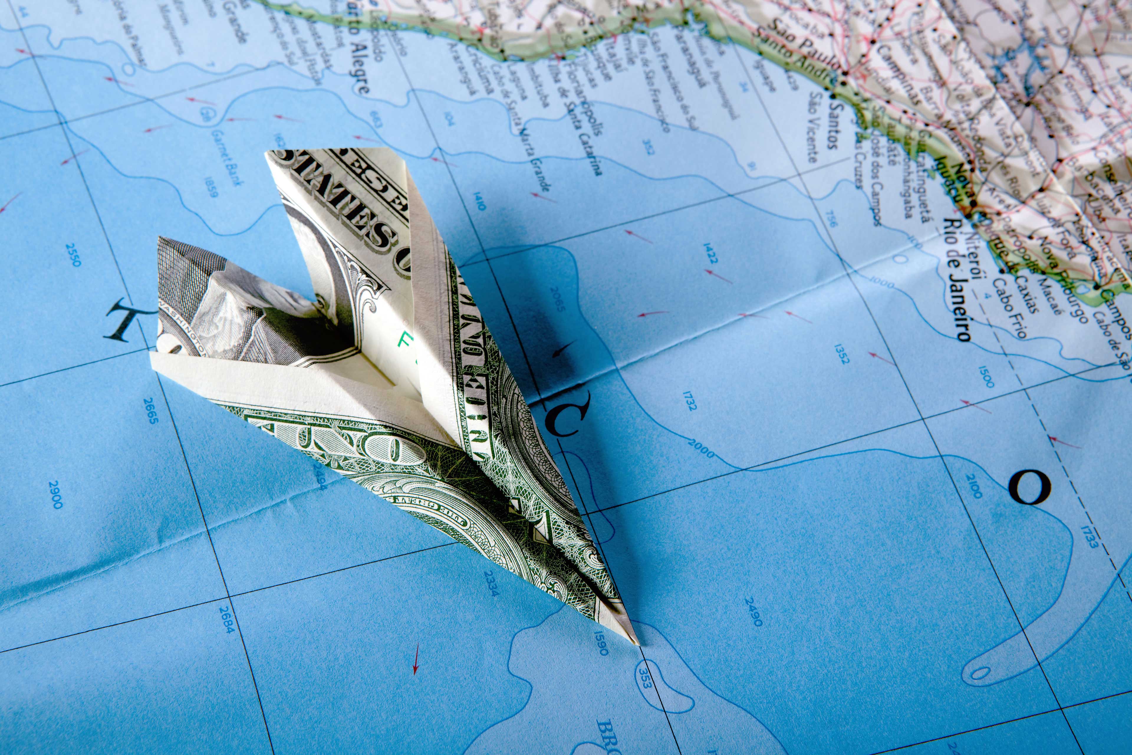 Paper plane made from dollar bill kept on top of map