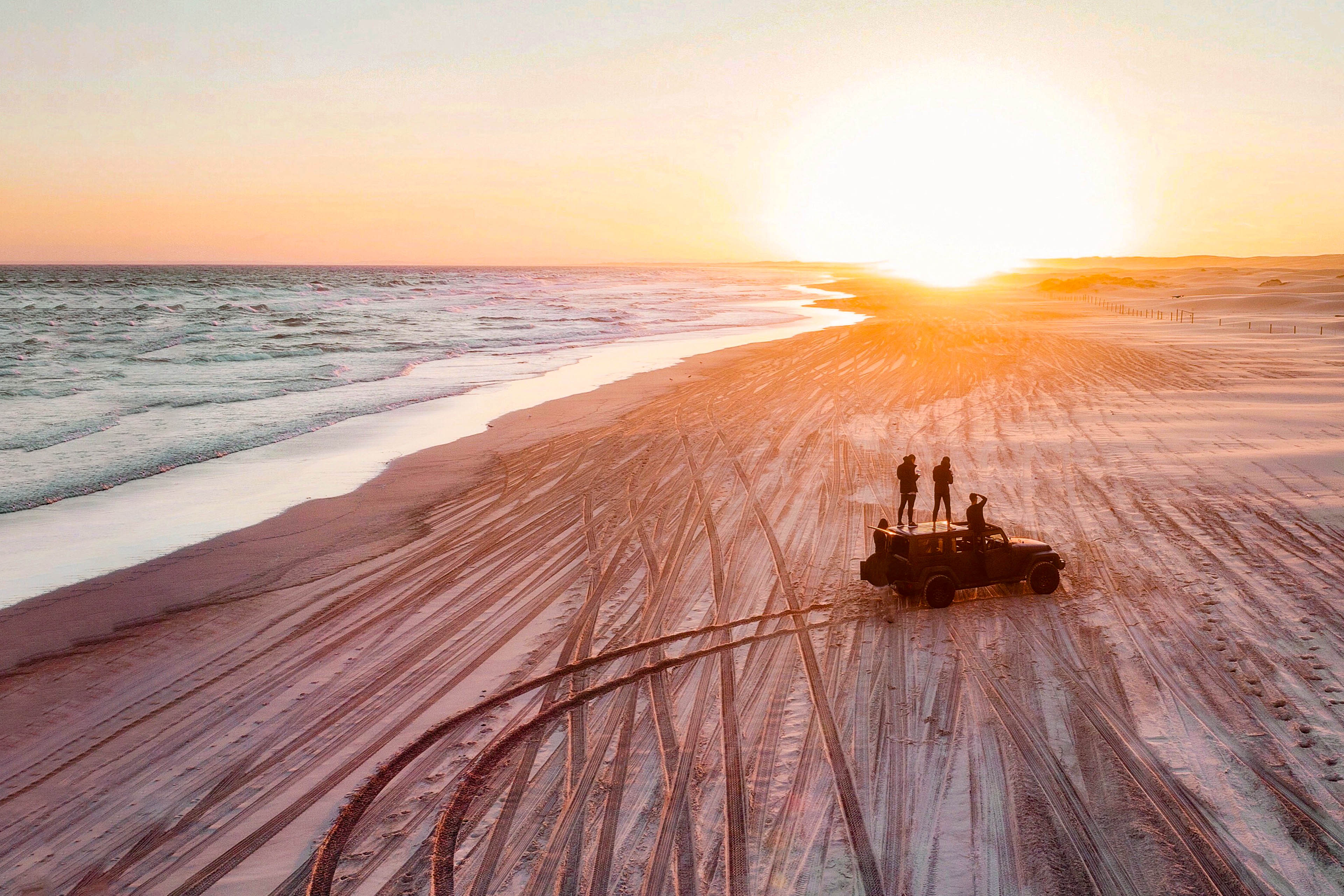 People watch the sunset by a 4x4 on the beach