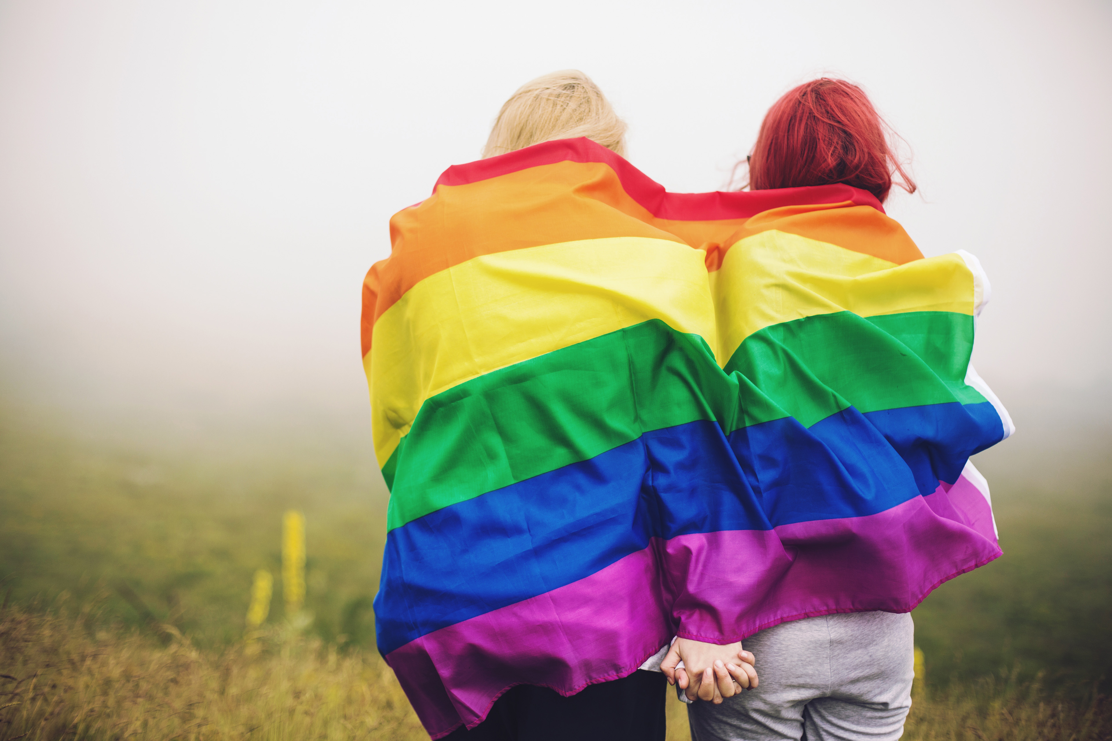 twee vrouwen omwikkelde regenboogvlag die elkaars hand vasthouden