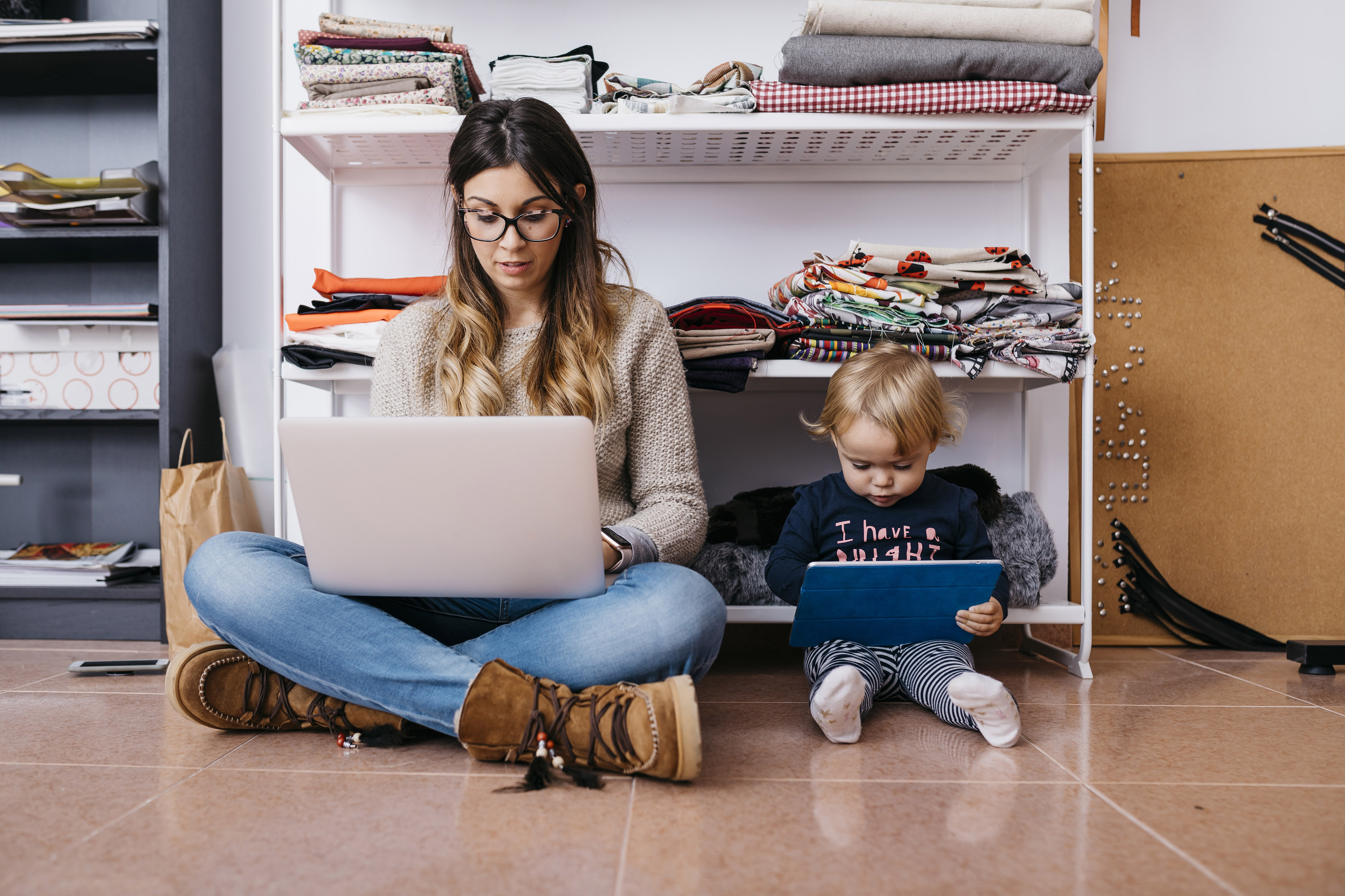 Mother and little daughter sitting on the floor at home using laptop and tablet