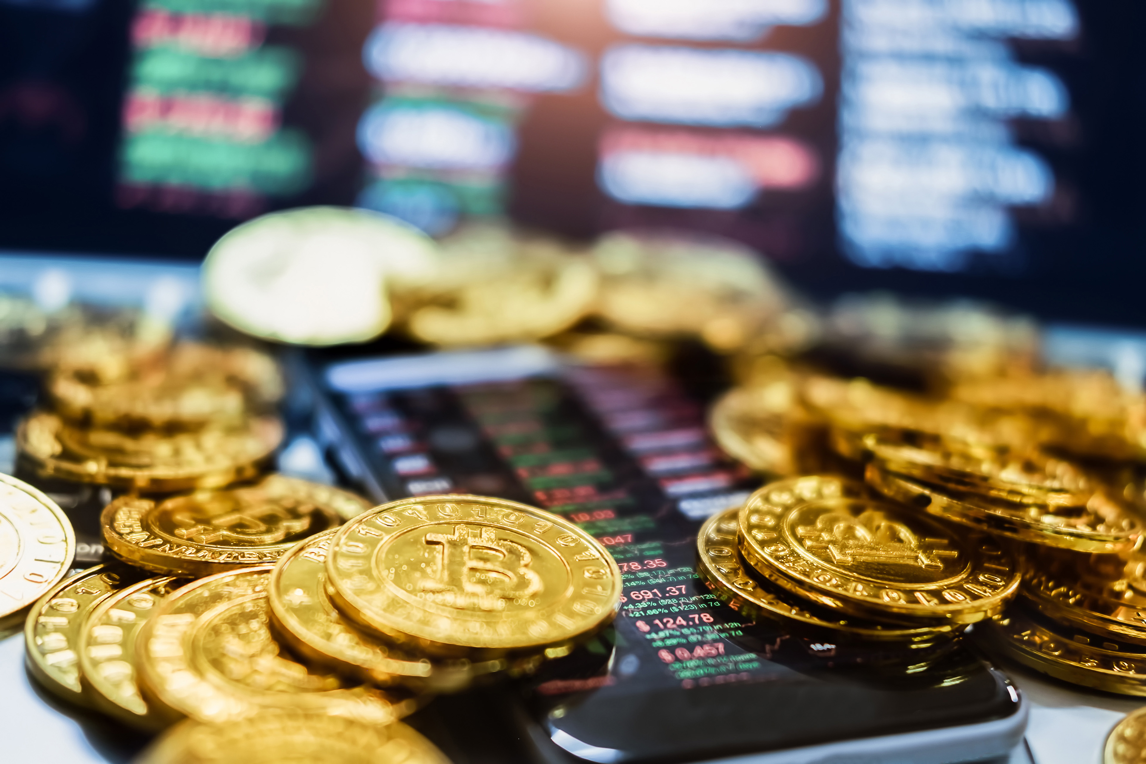 Crypto coins lying on a desk by a computer screen and an iphone