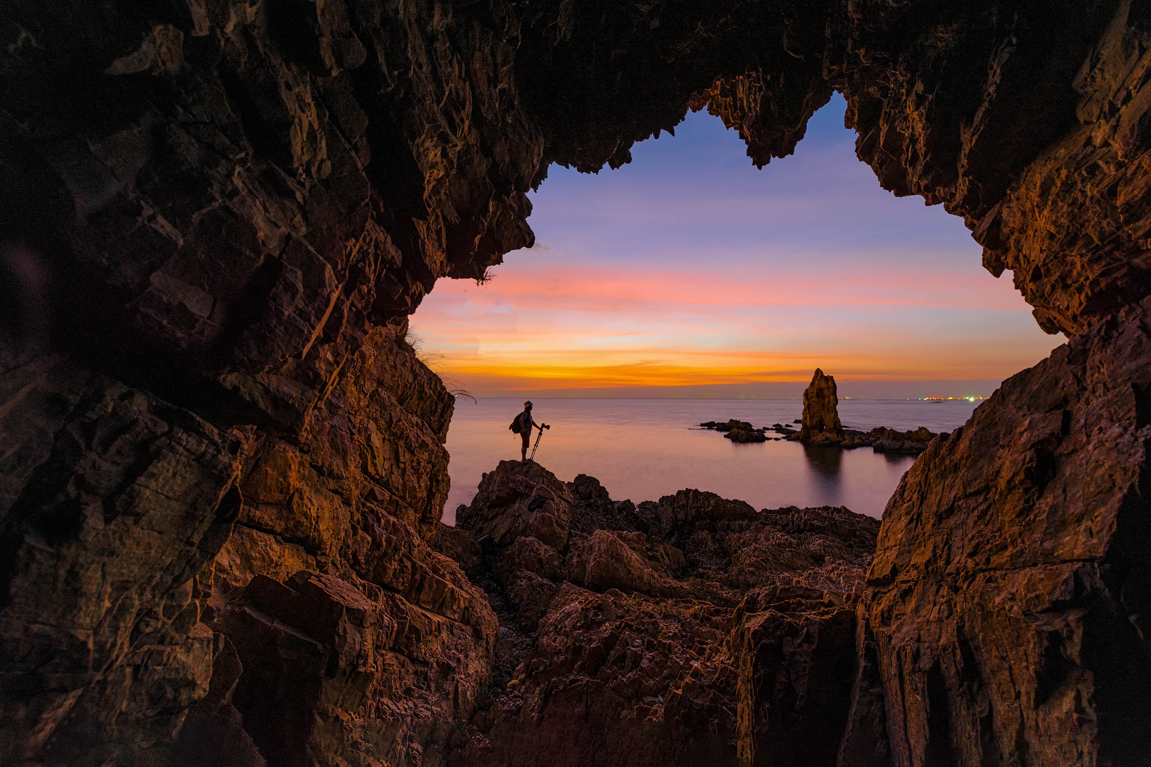 EY fotógrafo fica em pé no arco da rocha ao pôr do sol