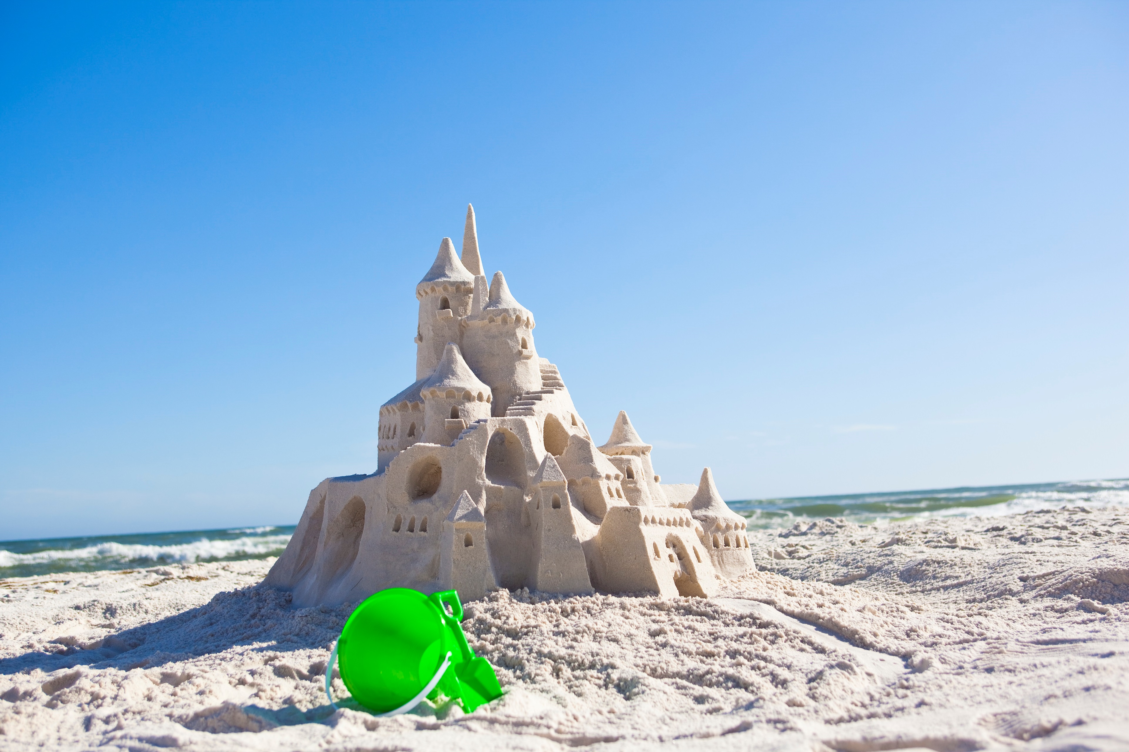 Elaborate sandcastle with towers on a beach, ocean waves in the background, and a clear sky.