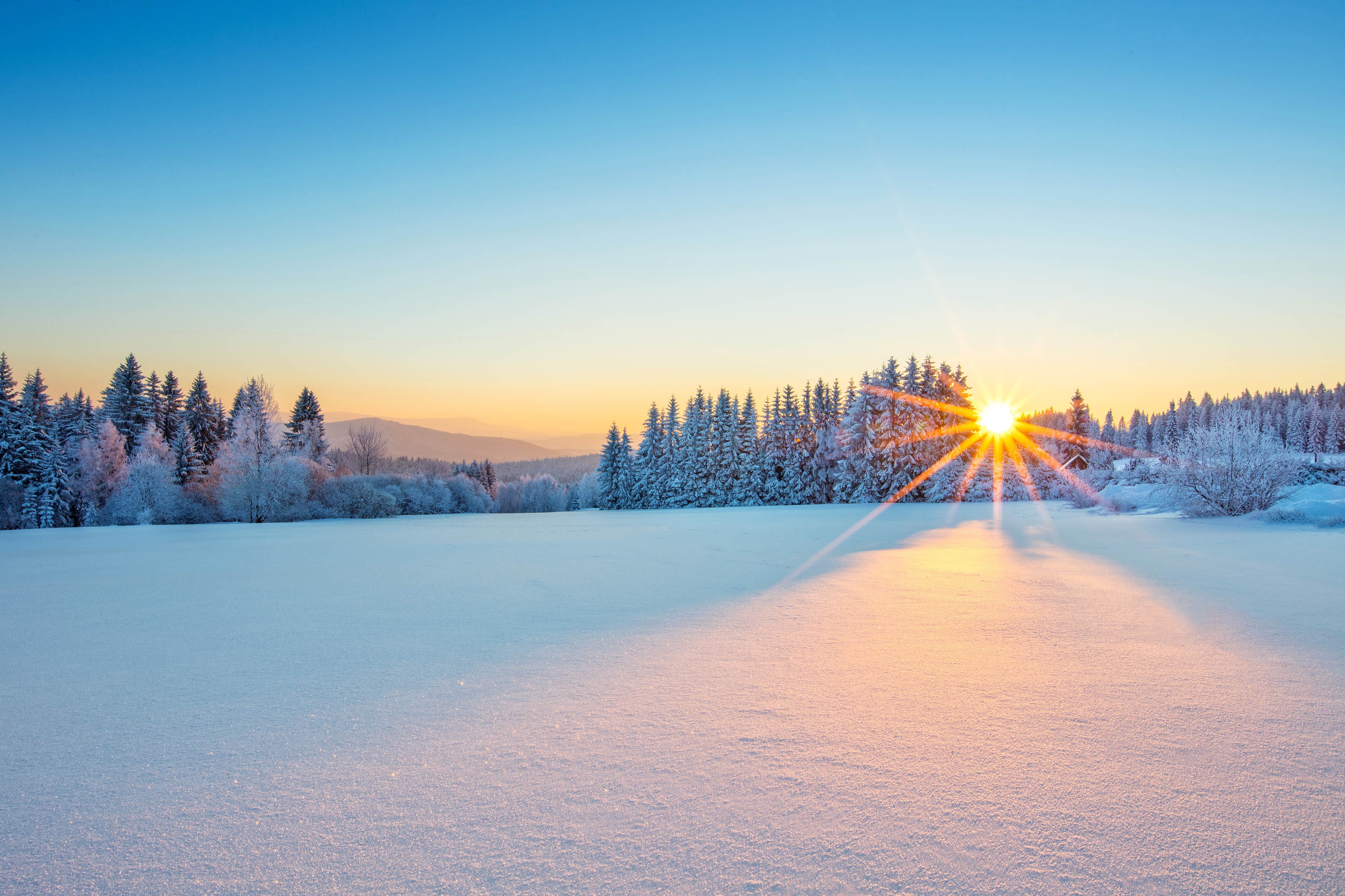 Ett vintervackert snötäckt landskap i solnedgång.