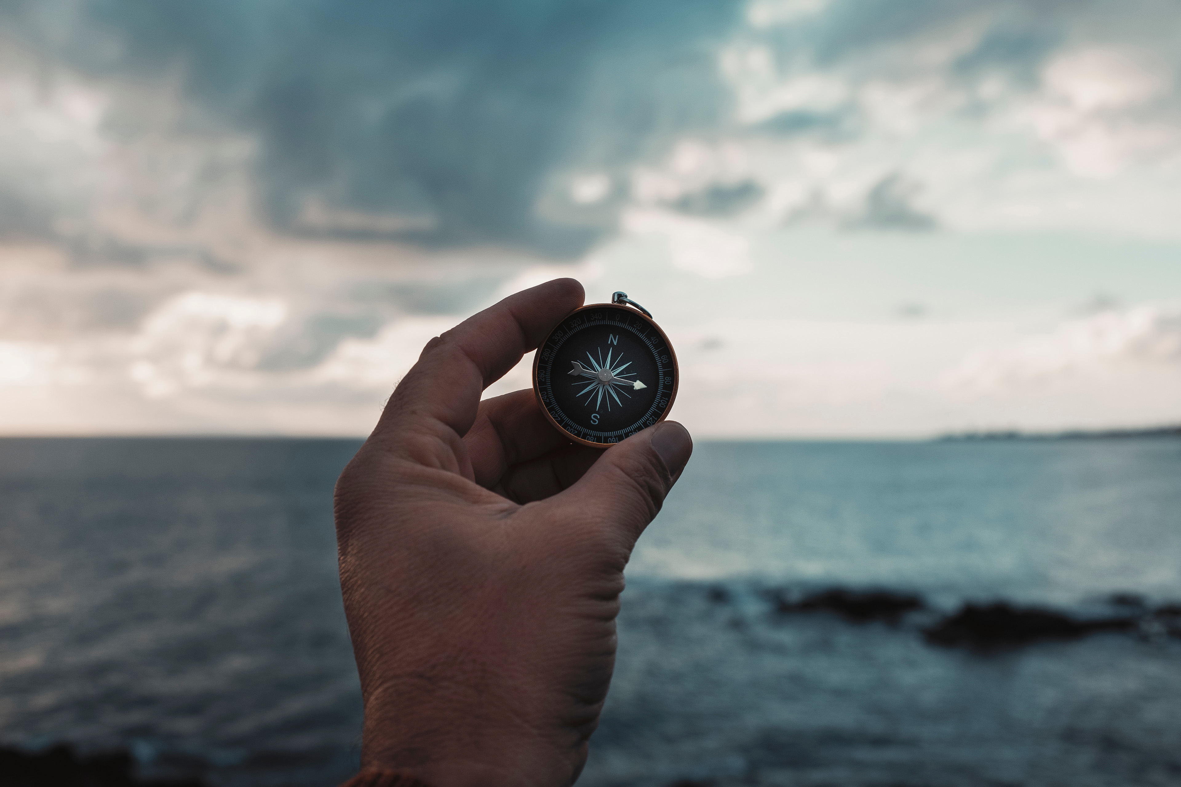 Pov of man hand holding navigational travel compass to find direction and next destination place. 