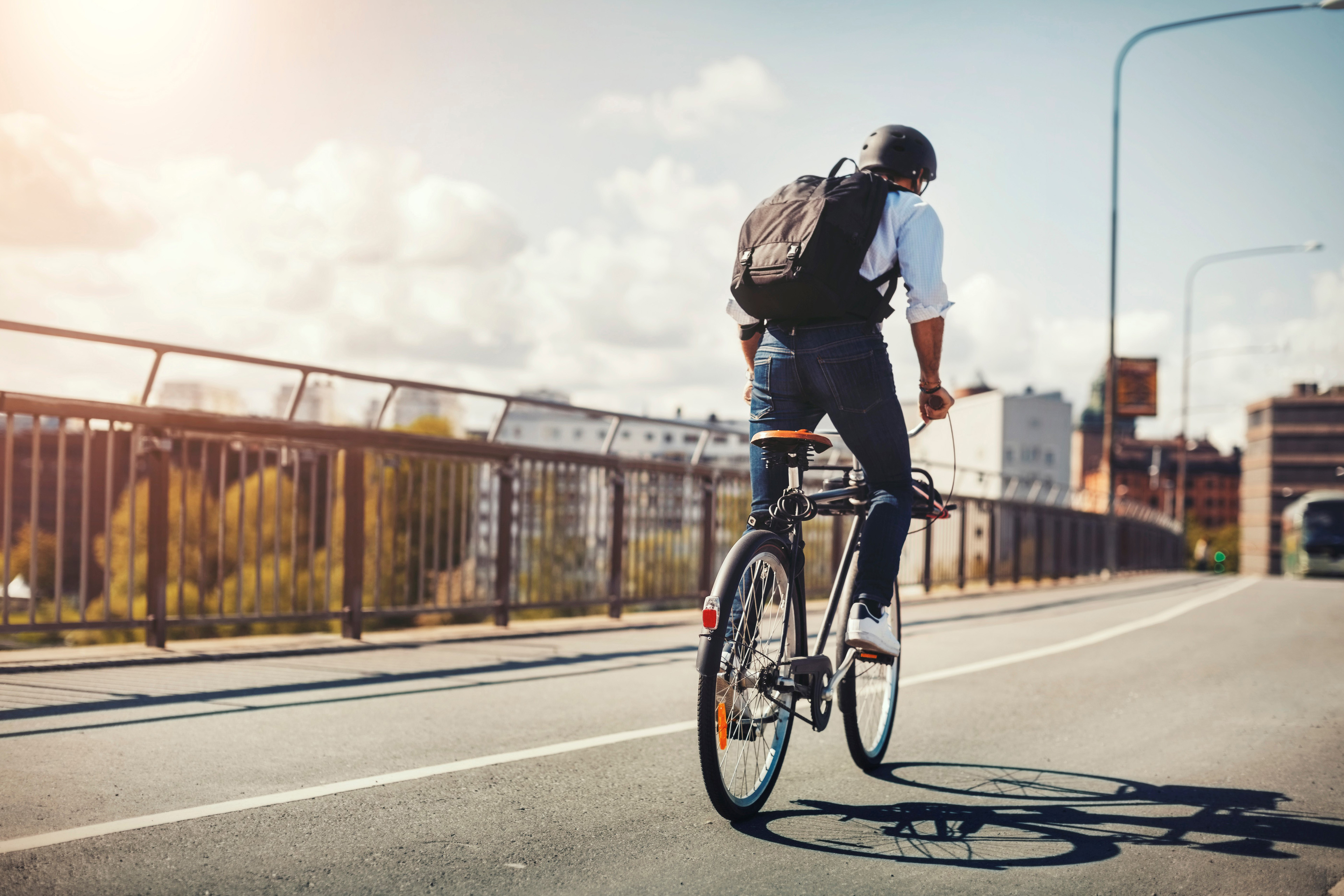 En man med ryggsäck sedd bakifrån cycklar över en bro