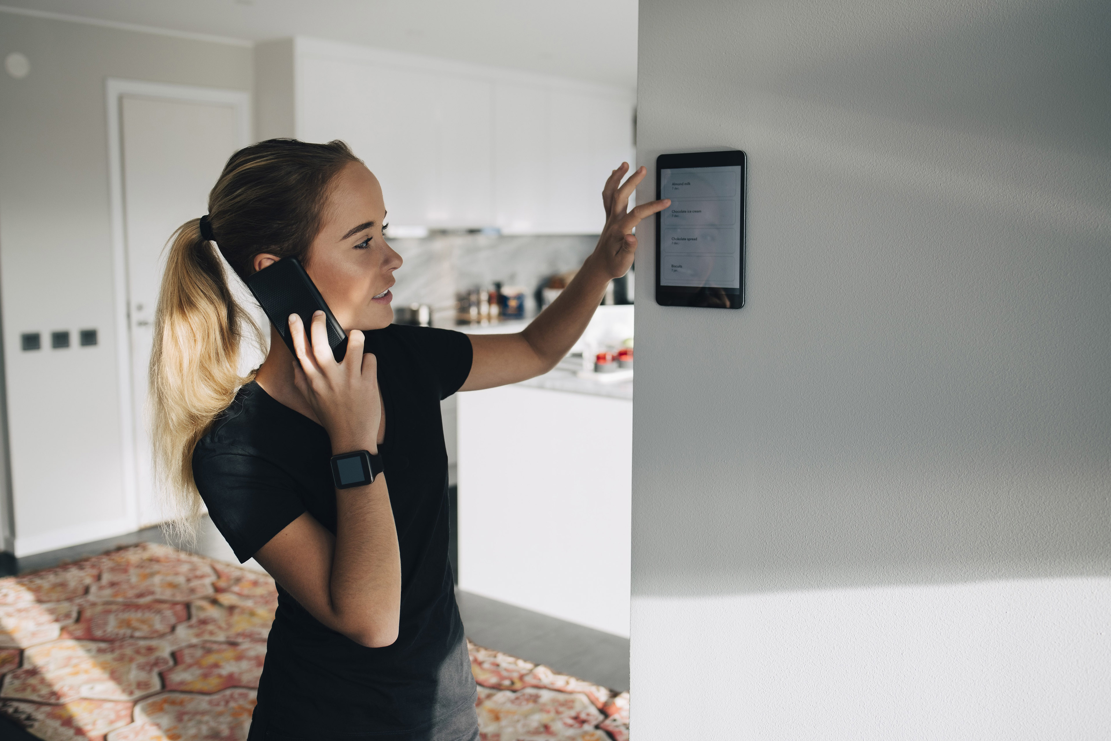 Tonårsflicka talar på mobiltelefon medan hon använder tablet fäst vid väggen