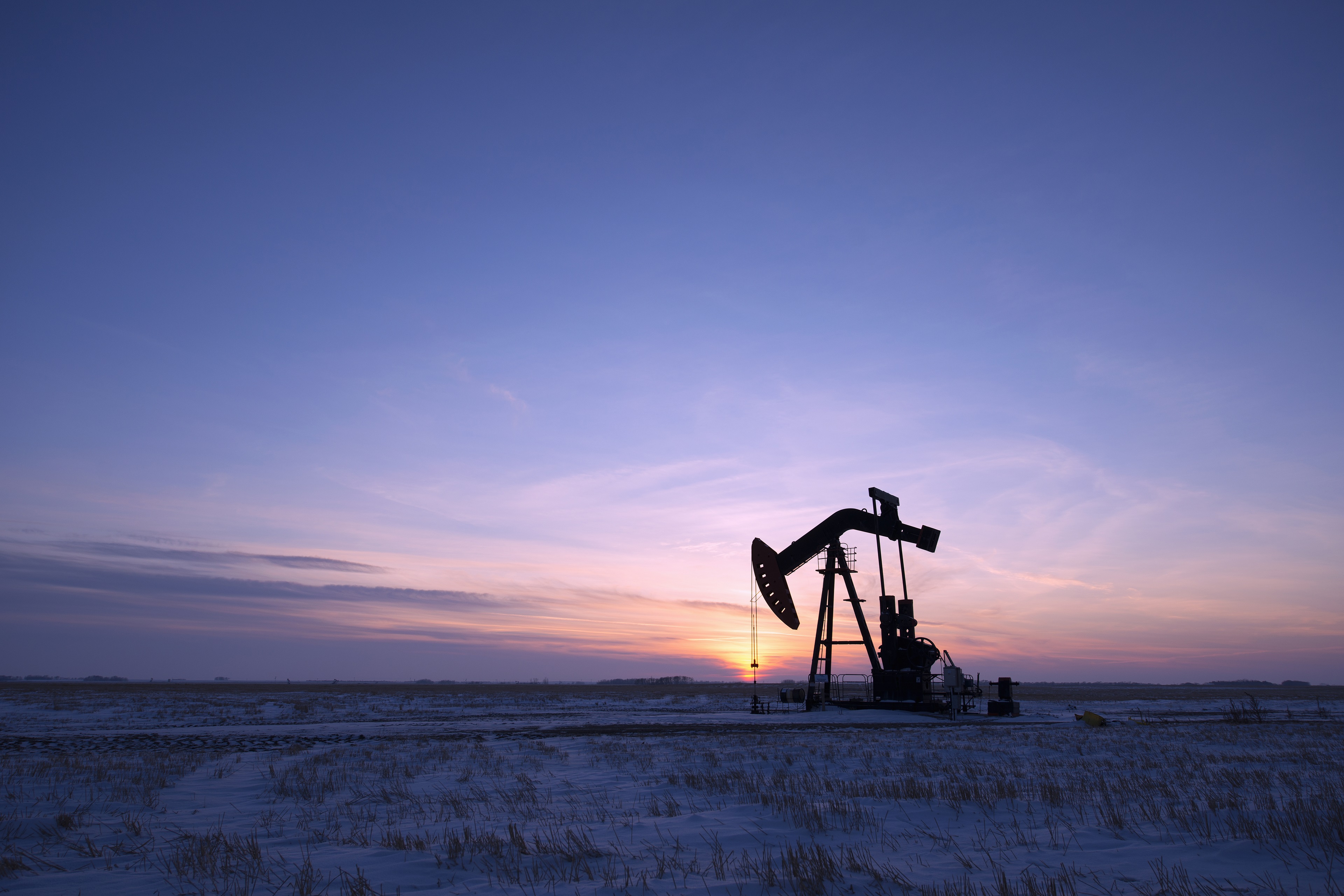 An oil drilling rig and pumpjack on a flat plain in the Canadian oil fields at sunset.