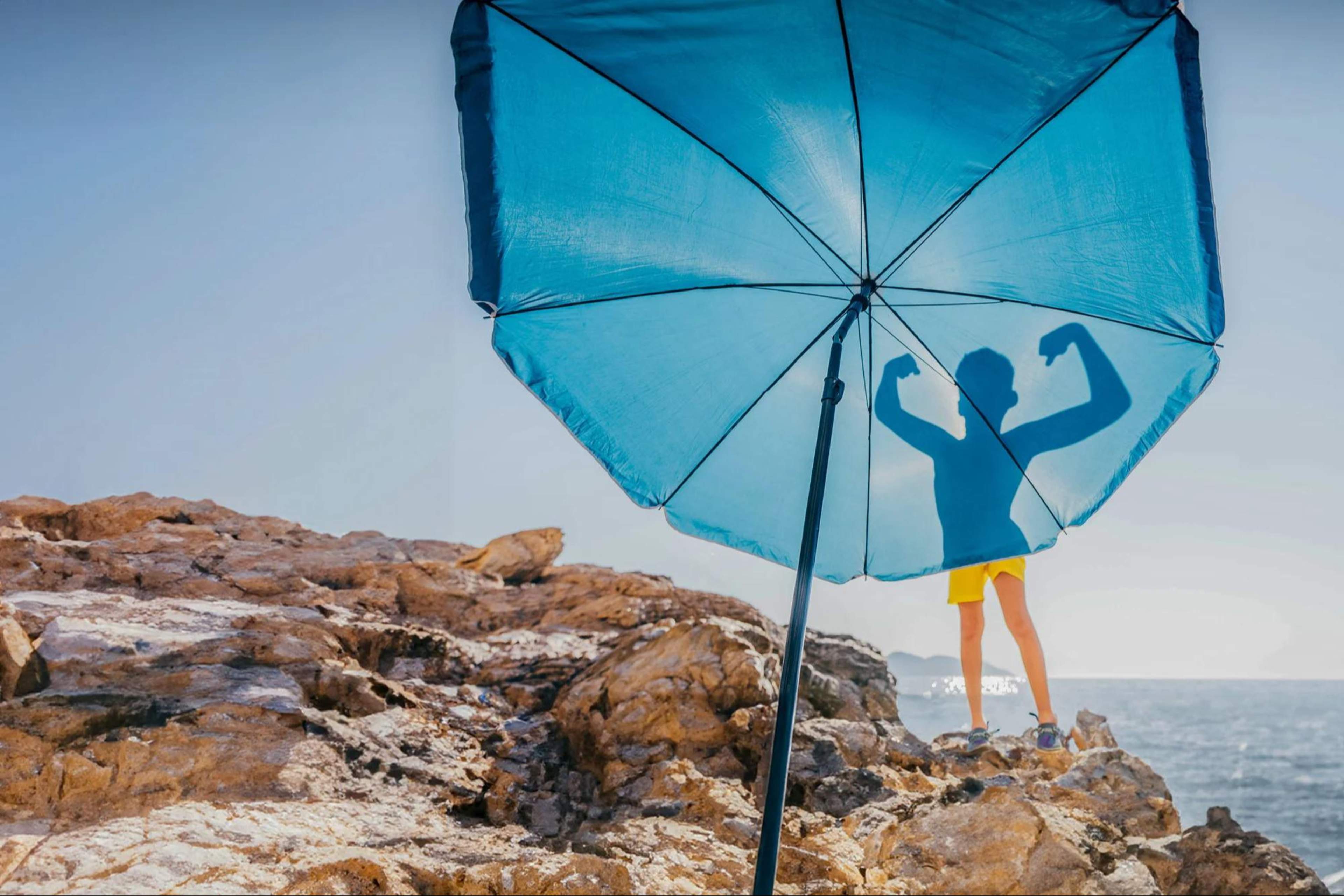 silhouette of boy flexing his muscles on blue beach umbrella hero