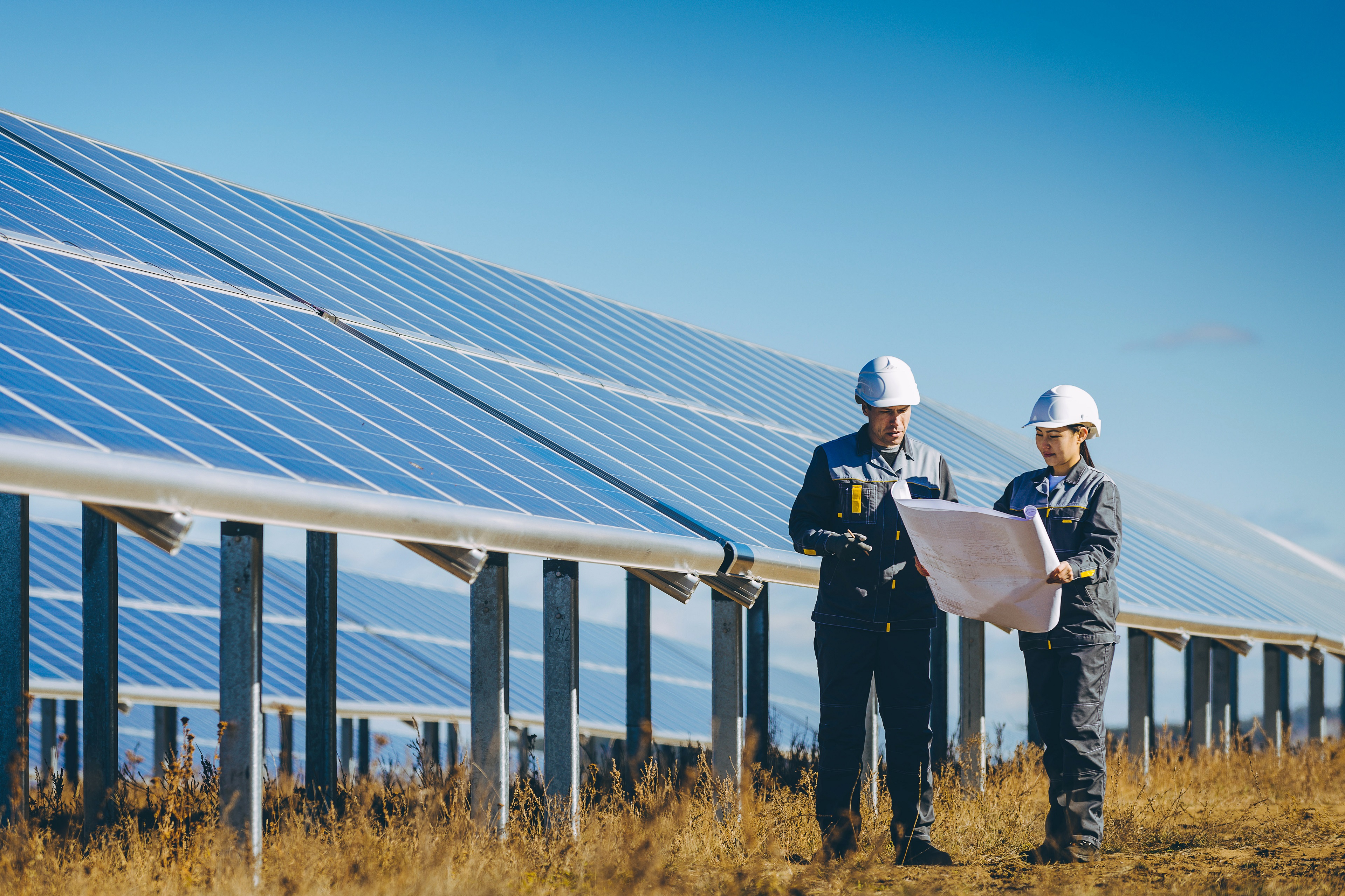 兩位工程人員站在太陽能發電廠內的大型太陽能模組旁研究工程文件。